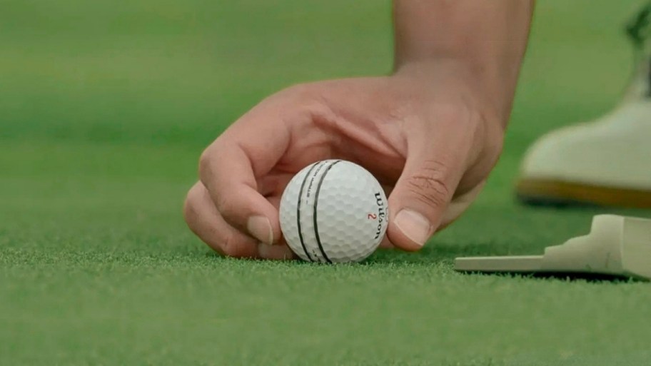 a mans hand placing a golf ball on a green next to a