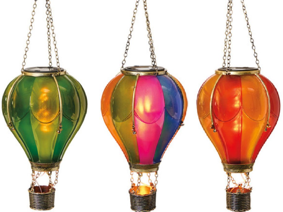 Three colorful lanterns shaped like hot air balloons hang in a row. Each has vibrant colors: green, blue-purple, and orange. Chains suspend them above.