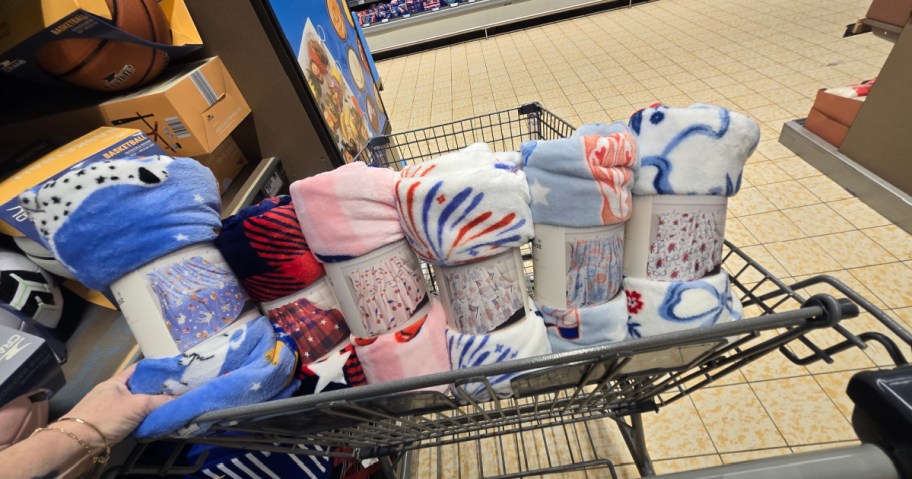 A shopping cart filled with colorful fleece blankets in various patterns, including blue, pink, and white designs.