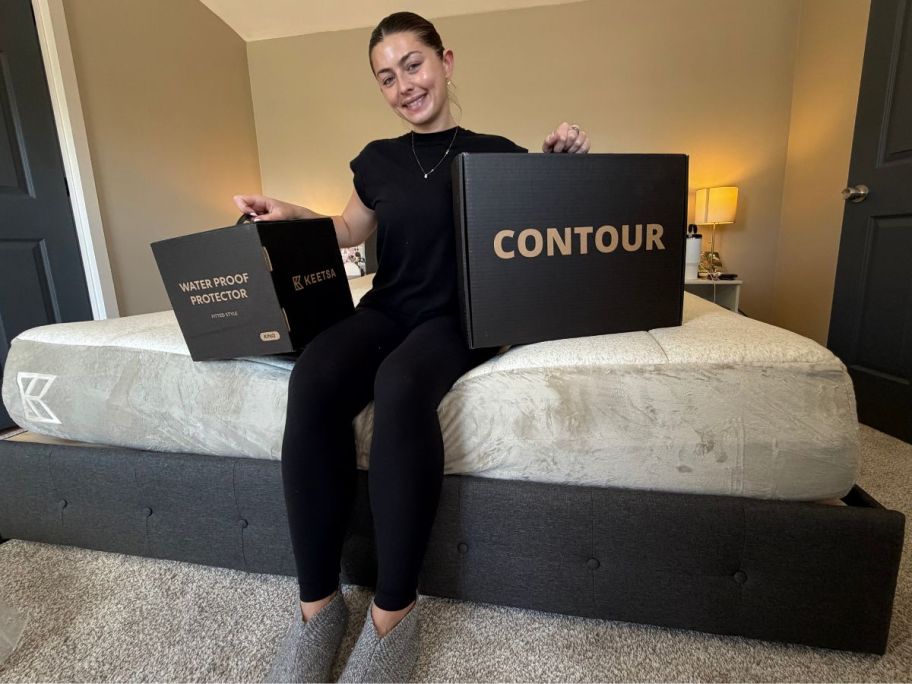 saylor sitting on Keetsa Tea Leaf Supreme Mattress holding 2 boxes
