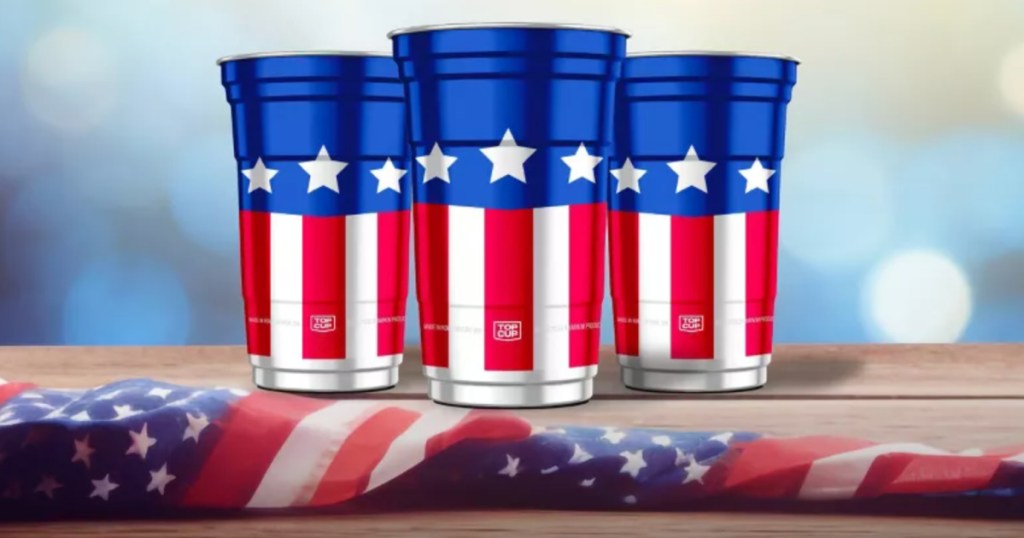 Red white and blue patriotic style aluminum cups on wooden table top next to American flag