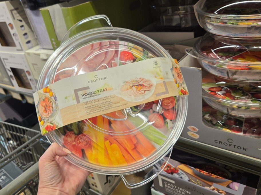 A hand holds a clear Crofton round tray with a lid.